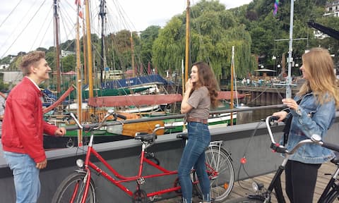 Junge Leute mit rotem Verleih Tandem vor dem Museumshafen.